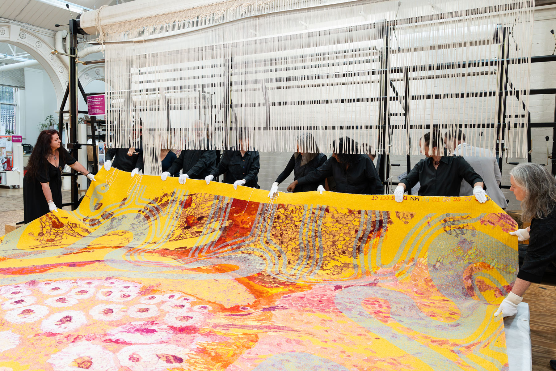 A large colourful tapestry is being cut of the loom