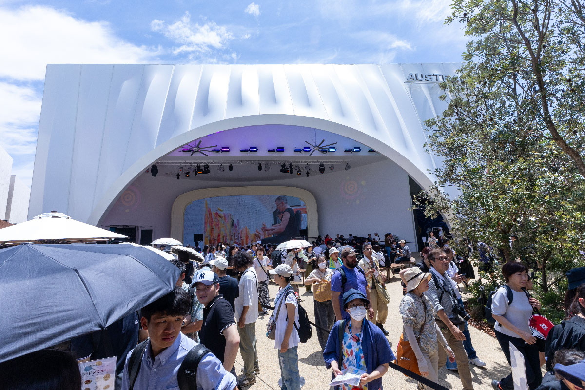 A group of people gather to rest in front of a large screen showing weaving in progress