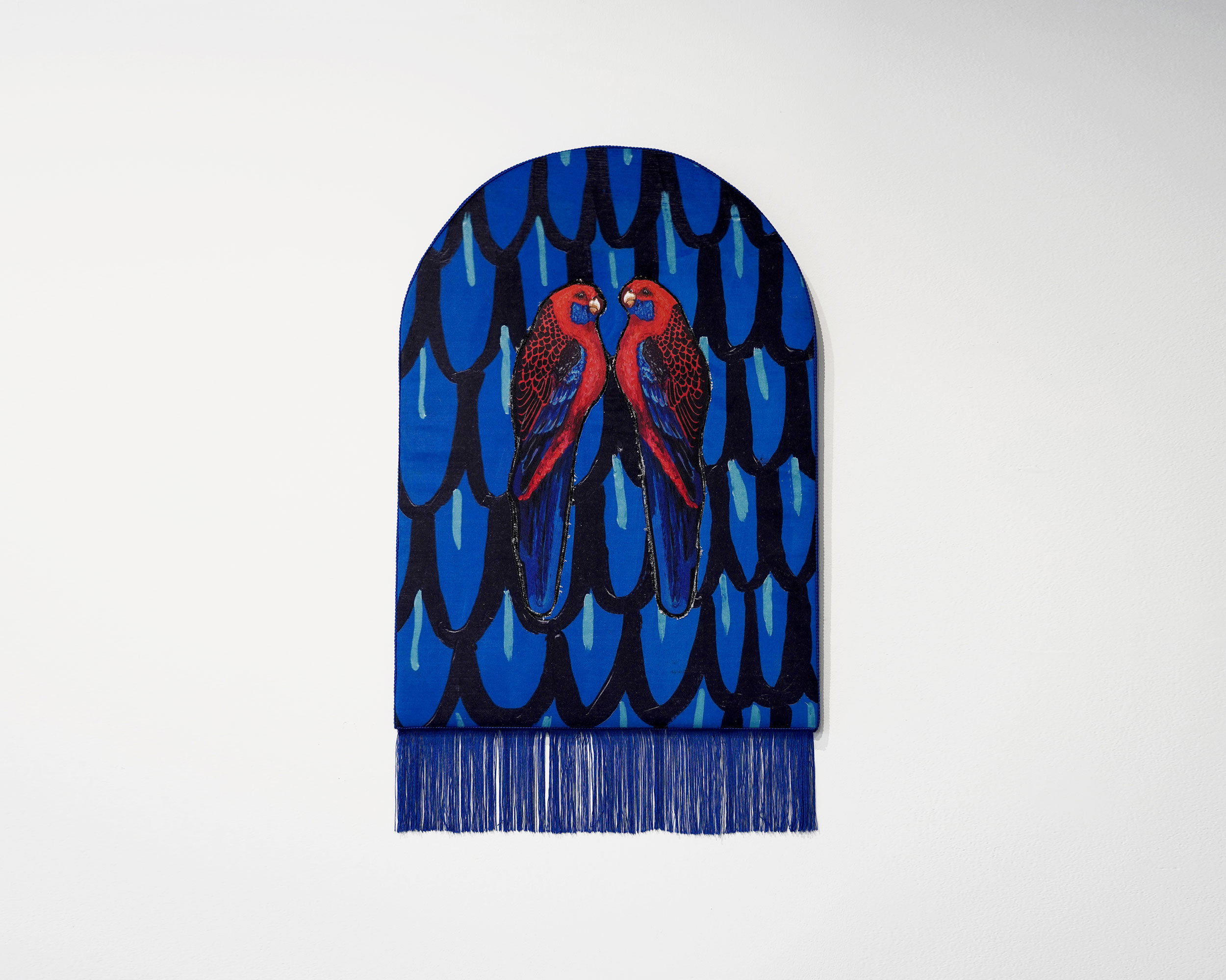 A vibrant blue textile artwork featuring a pair of rosellas