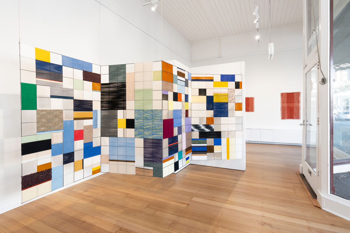 Installation view of Jacqueline Stojanović's artwork featuring coloured yarn wound around wide metal mesh, forming a vibrant, grid-like structure.